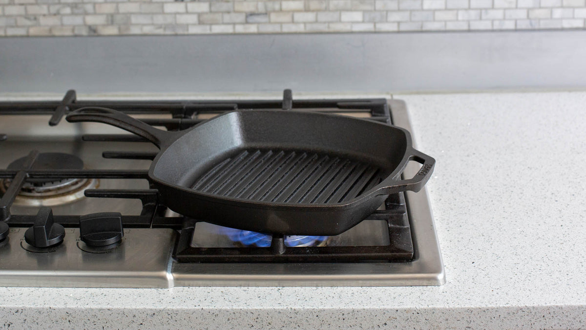 Lodge square black grill pan with handle and textured cooking surface, 26.7 cm diameter for grilling and searing.