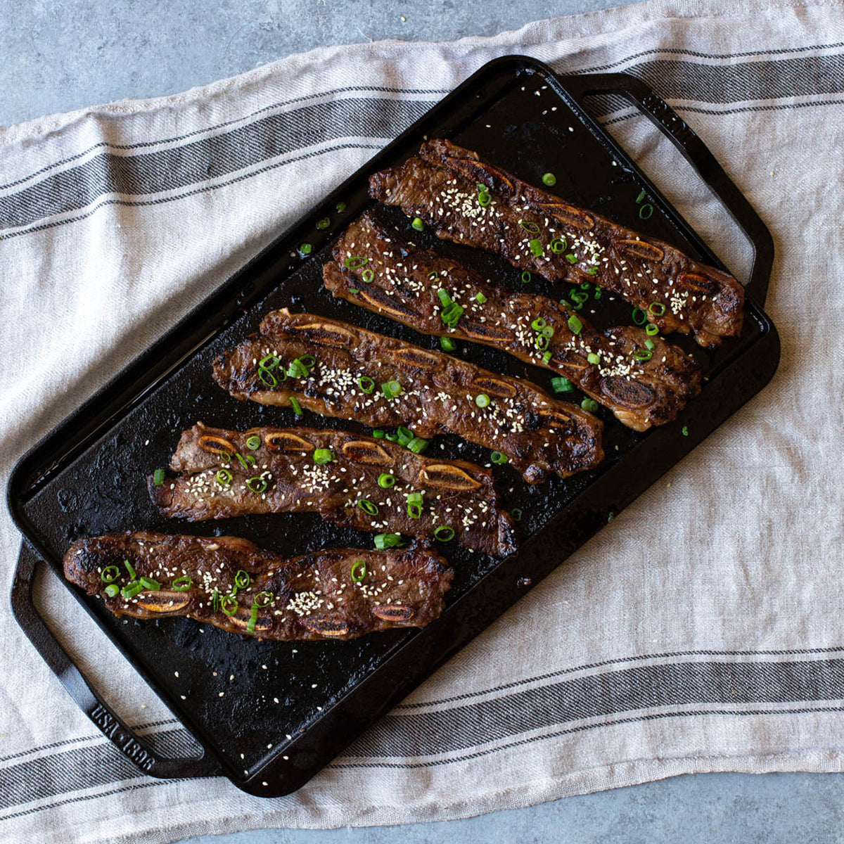 Lodge 2-sided grill plate with smooth and ridged surfaces, 50.8 cm x 25.4 cm for versatile outdoor cooking.