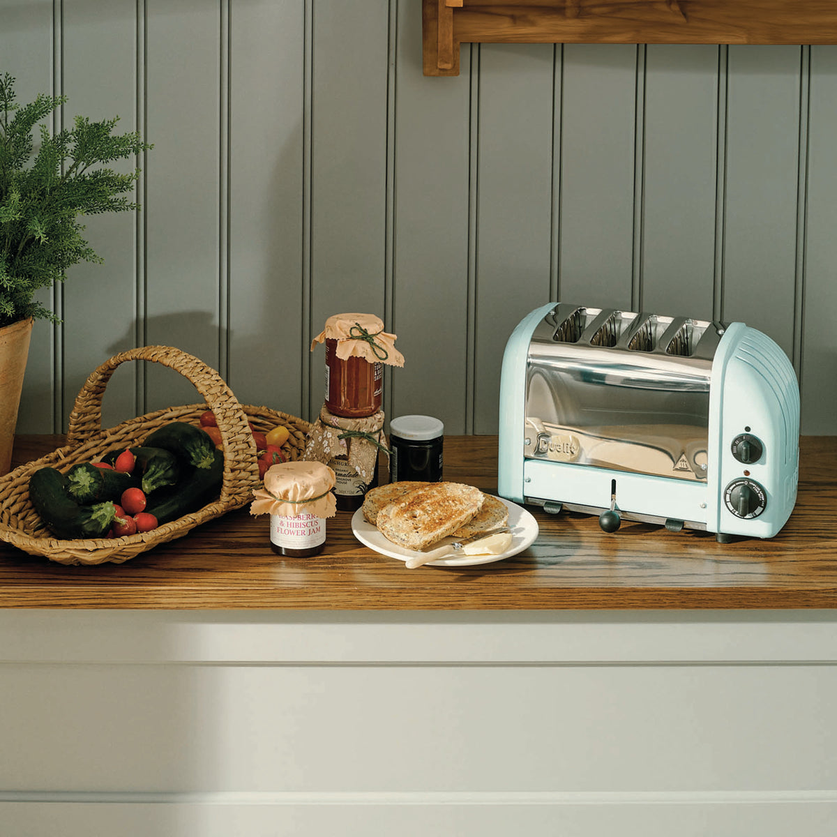 Dualit Newgen blue 4-slice toaster with modern design and control knobs, visible on a kitchen countertop.