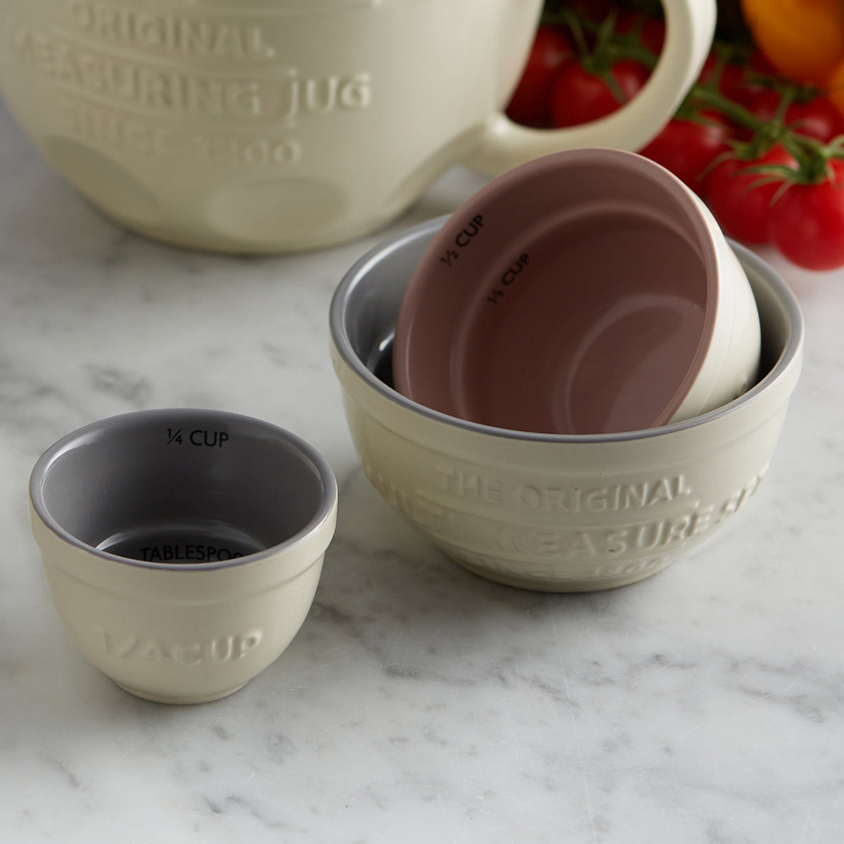Set of four white Mason Cash measuring cups, stainless steel handles, arranged in a stack with clear measurement markings.