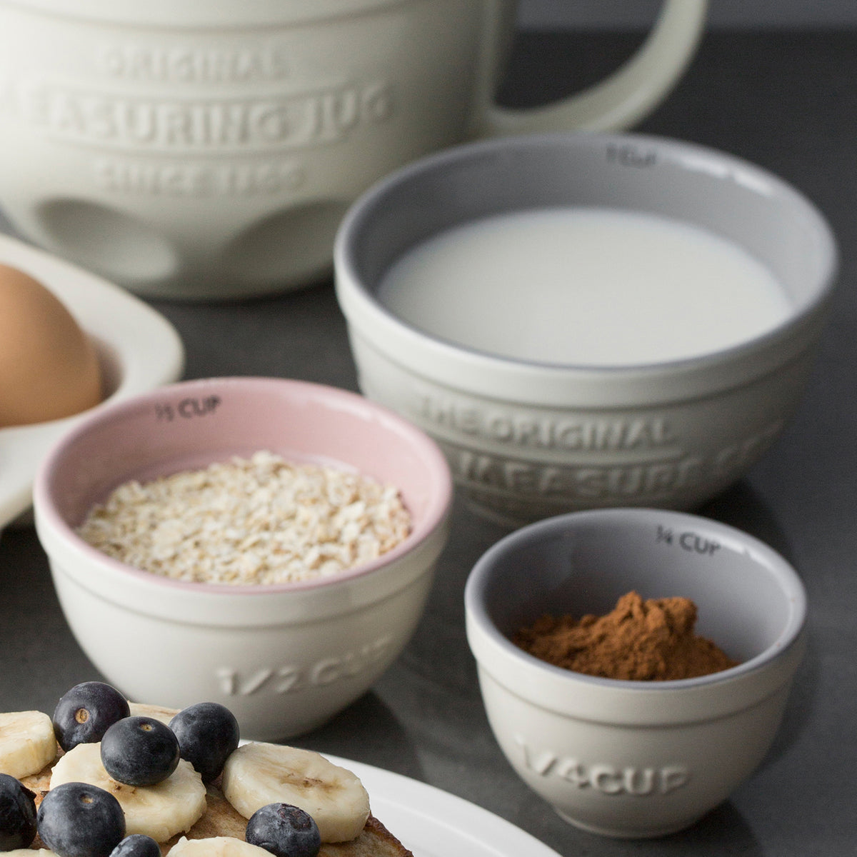 Set of four white Mason Cash measuring cups with clear markings, designed for accurate liquid and dry ingredient measurement.