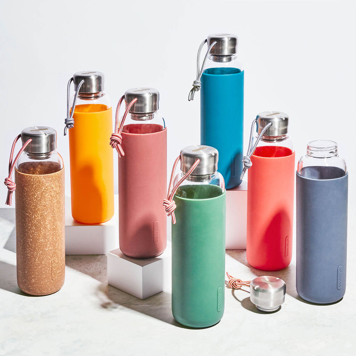 BLACK+BLUM TO-GO GLAS water bottle in ocean blue, 600ml, with a sleek glass design and black silicone sleeve for portability.