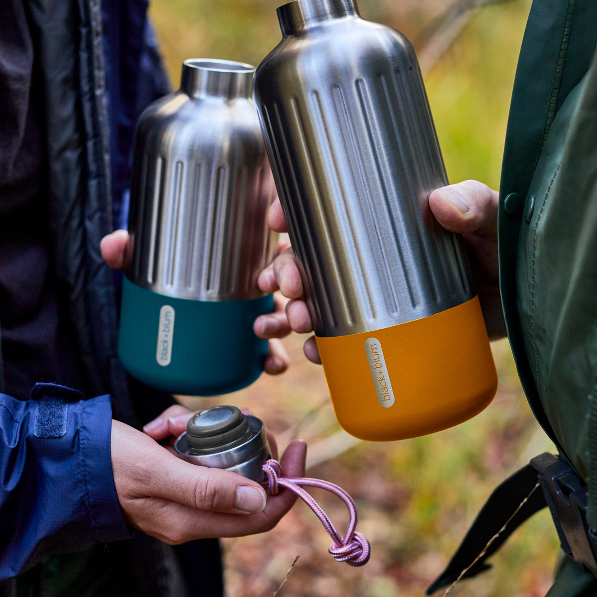 BLACK+BLUM Explorer insulated bottle in vibrant orange, designed for hiking and outdoor adventures, shown in a lifestyle setting.