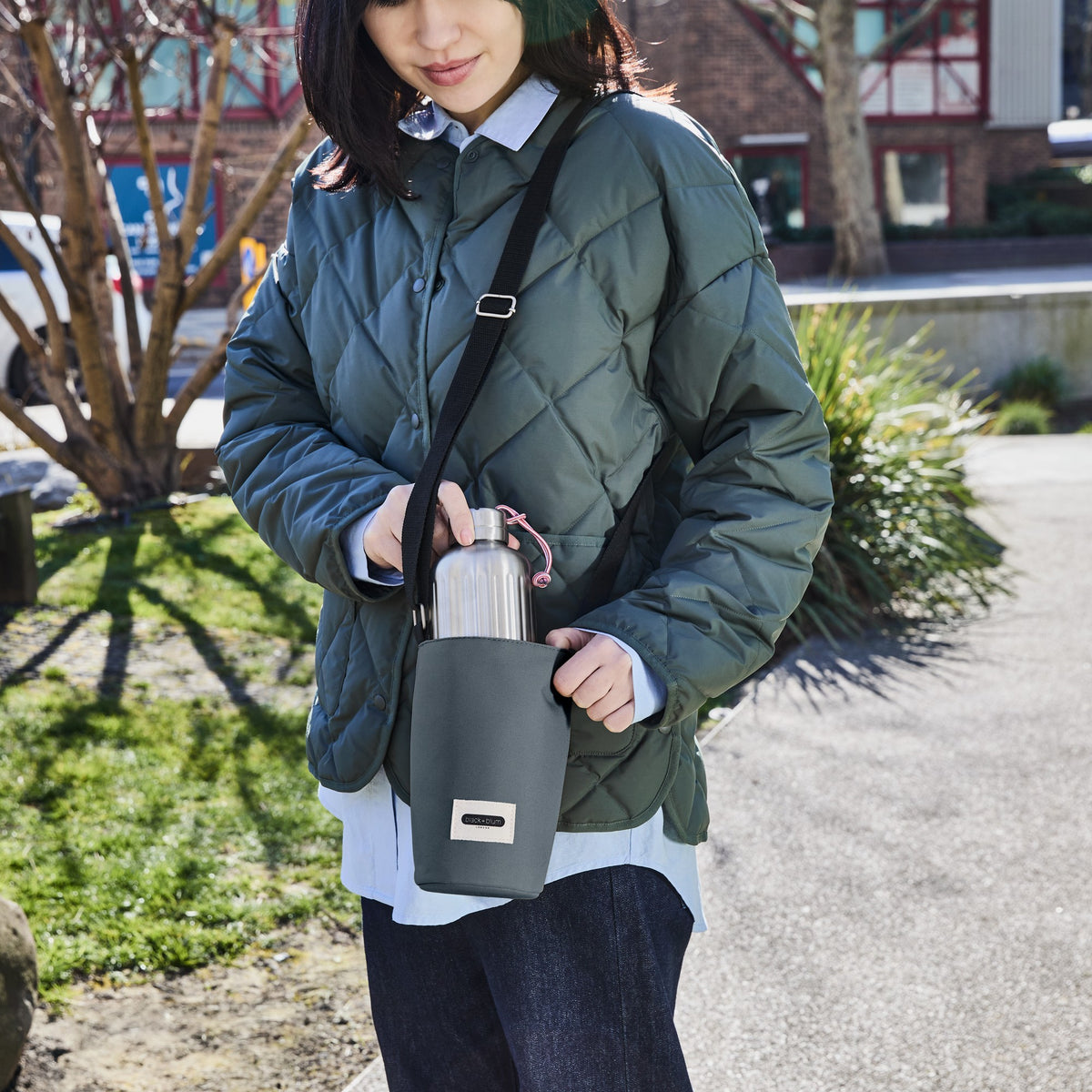 Black+Blum bottle bag in slate, outdoor city scene, designed to carry and protect glass or plastic bottles.