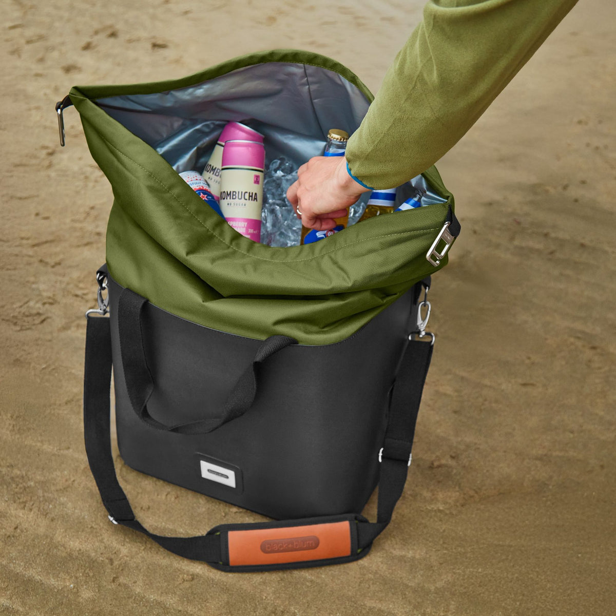Black+Blum insulated cooler bag, foldable and moss green, shown open with interior storage for snacks and beverages.