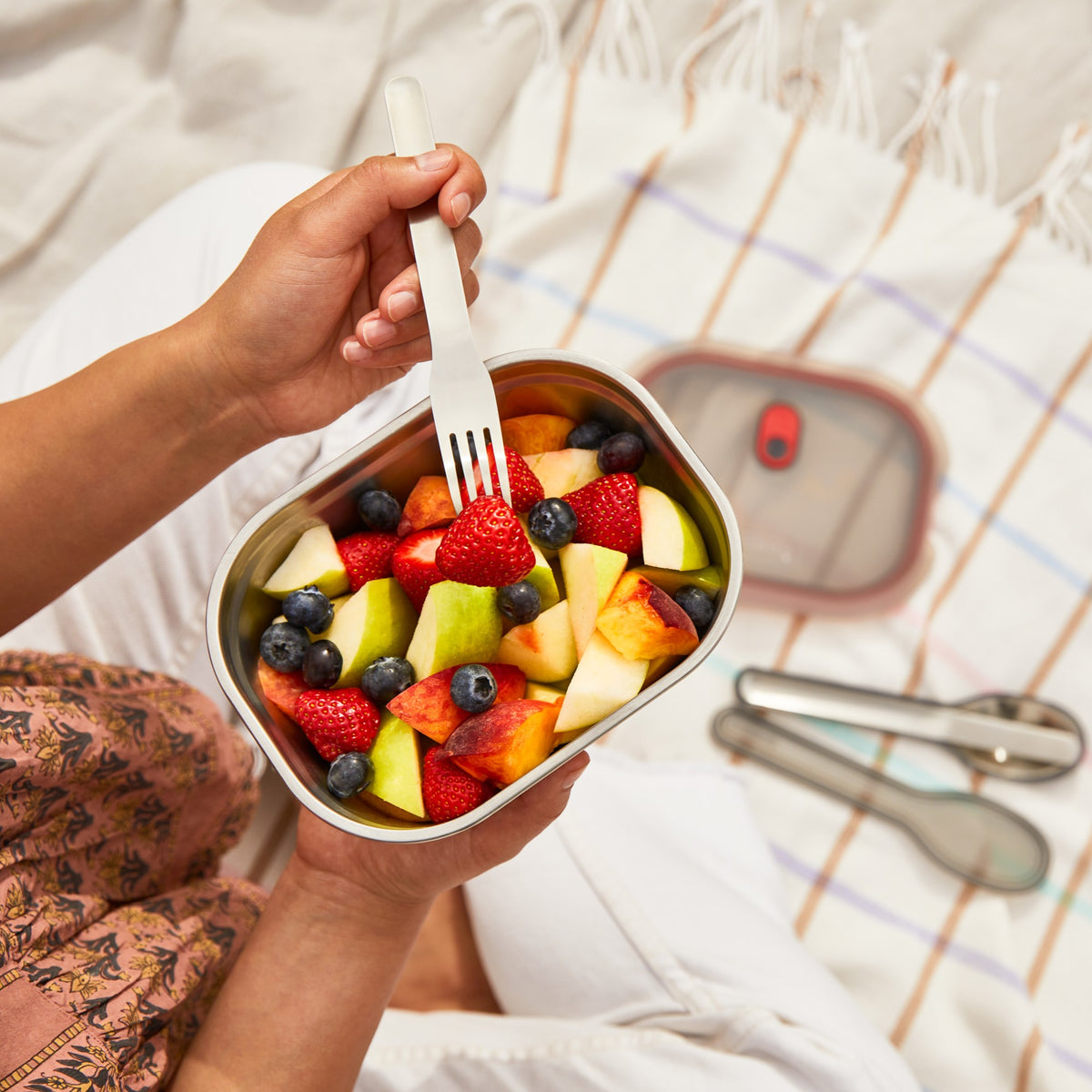 Black+Blum stainless steel multifunction storage container with a rectangular shape, shown filled with fruit and salad.