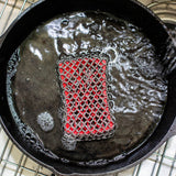 Lodge silicone and steel scrub pad in red for cleaning cookware, shown in a close-up image.