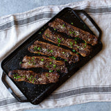 Lodge 2-sided grill plate with smooth and ridged surfaces, 50.8 cm x 25.4 cm for versatile outdoor cooking.