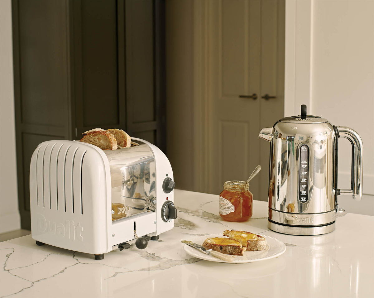 Dualit Newgen white 2-slice toaster with modern design and adjustable browning control, shown with toasted bread slices.
