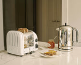 Dualit Newgen white 2-slice toaster with modern design and adjustable browning control, shown with toasted bread slices.