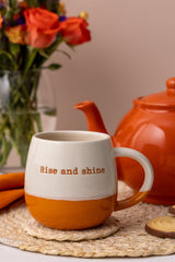 Orange ceramic tasse with "Rise and Shine" text from Price & Kensington, featuring a cheerful design and bold colors.
