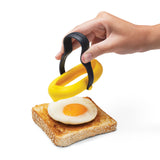 DREAMFARM Spiegelei-Heber 2er Set in yellow, kitchen egg poachers for perfect fried eggs, shown in use on a frying pan.