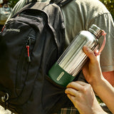 BLACK+BLUM Explorer insulated bottle in orange, 850ml, shown in backpack with olive fabric, designed for hot and cold beverages.
