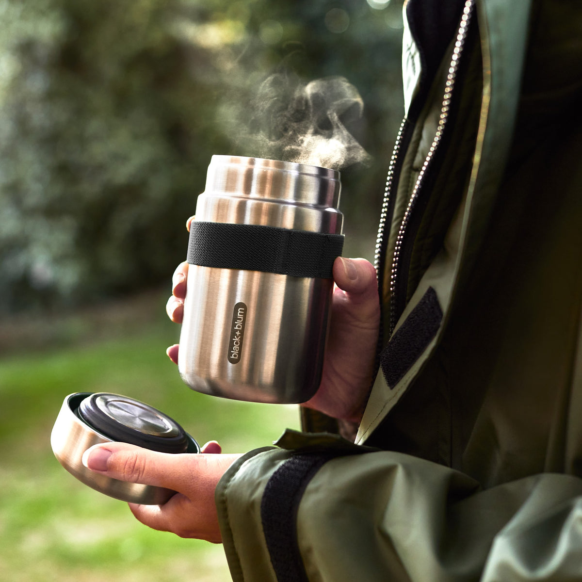 Black+Blum food flask in black with orange lid, open outdoors showing its insulated interior for keeping food fresh.