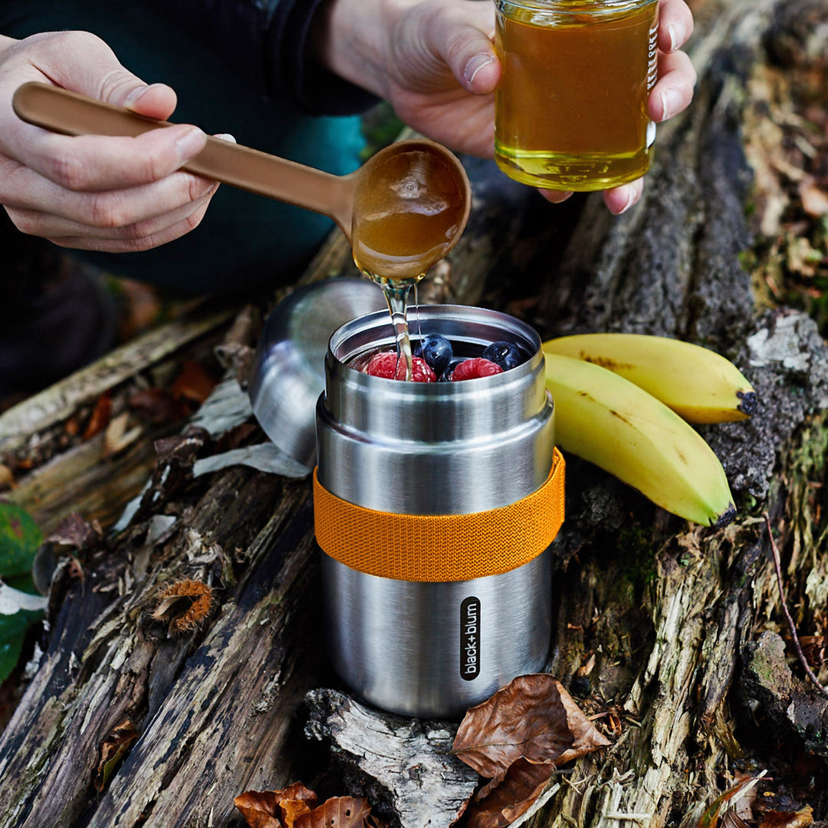 Black+Blum food flask in orange, open with fresh fruit inside, ideal for lunch and outdoor activities.