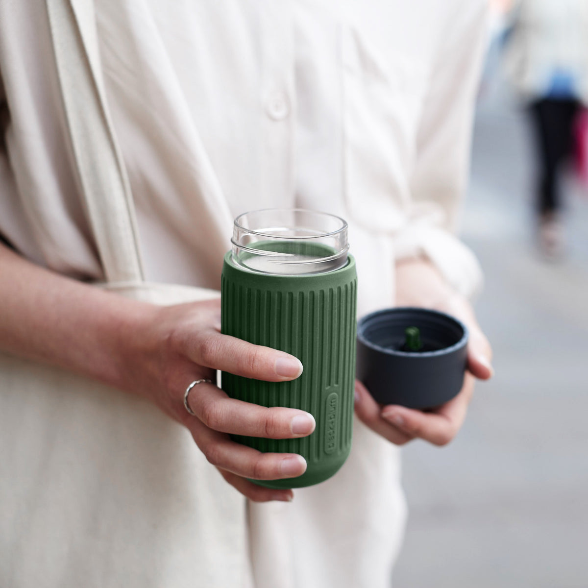 BLACK+BLUM blue to-go coffee cup with clear glass body and black lid, open with coffee inside.
