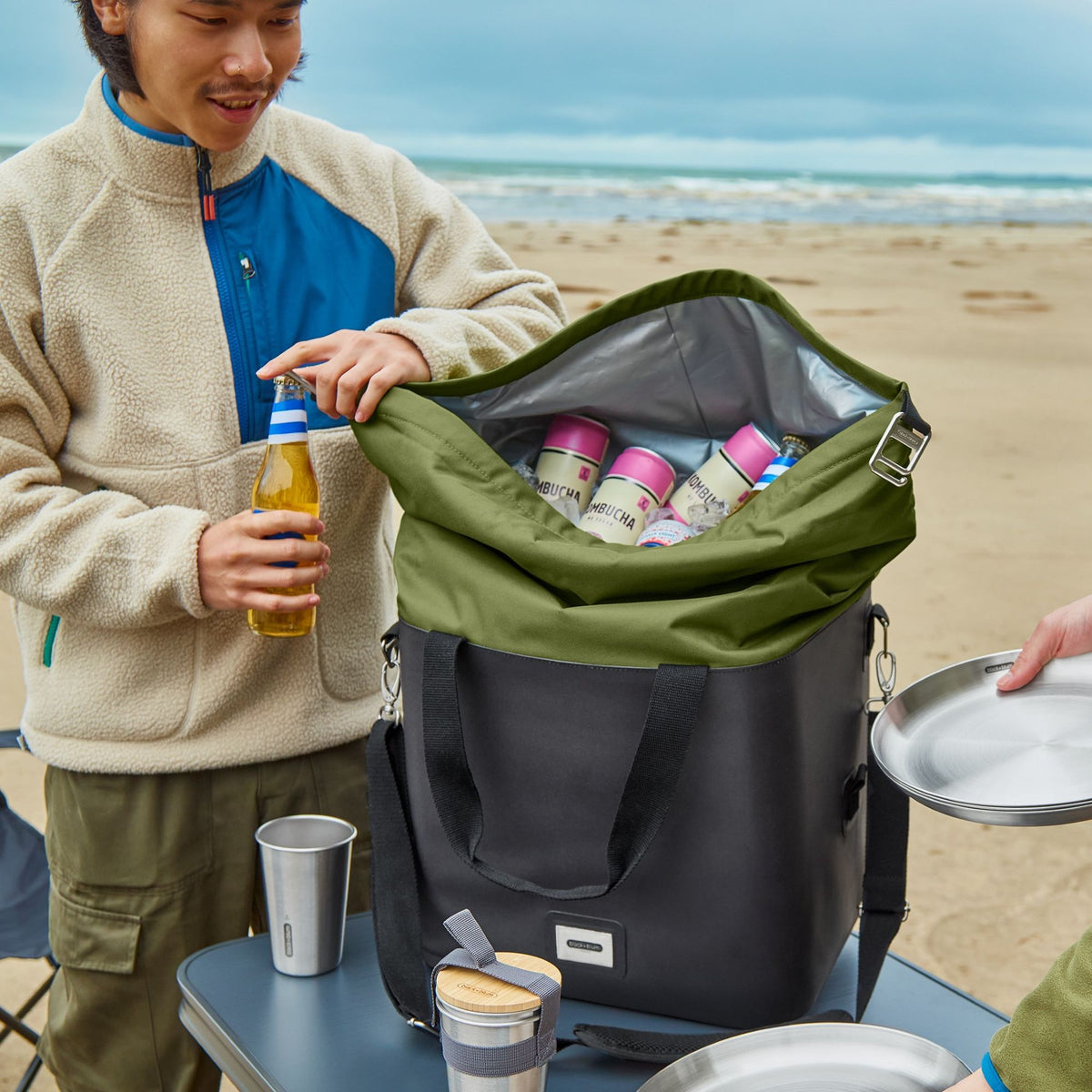 Black+Blum insulated cooler bag in moss color, open to show spacious interior and included bottle opener, ideal for beach outings.