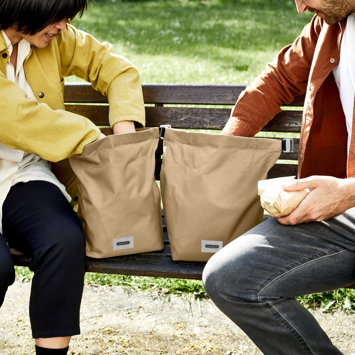 Black+Blum lunchbag with clay exterior, open to reveal lunch inside, designed for portability and style in a park setting.