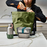 Black+Blum insulated lunchbag open on a counter, showing interior space and moss-green accents, designed for carrying meals comfortably.