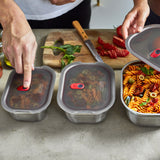 Set of three BLACK+BLUM stainless steel multifunction storage boxes, closed with people in the background.