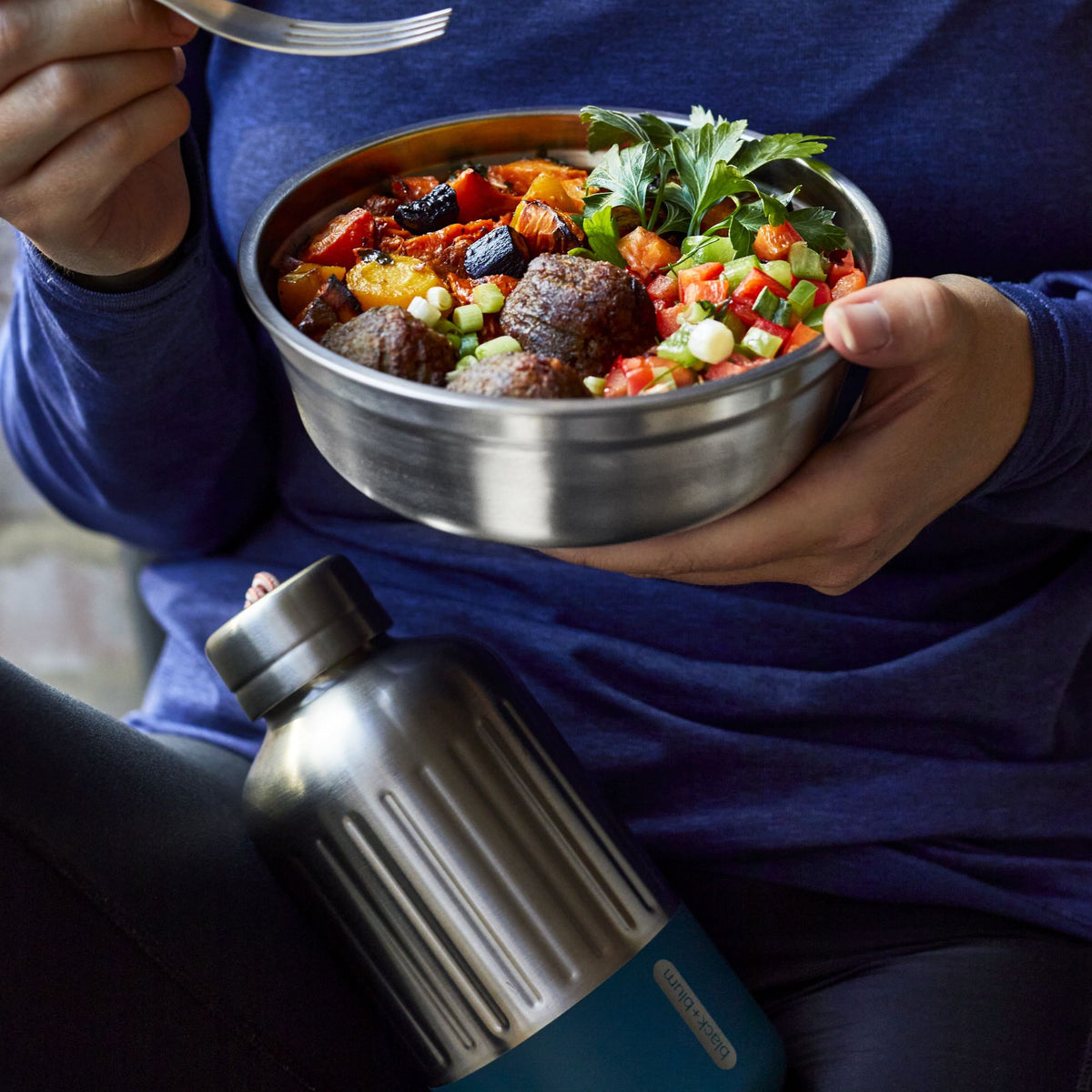 BLACK+BLUM stainless steel multifunctional storage container with a woman eating from a small bowl.